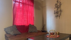 A living room with a brown sofa, red curtains, a decorative wall piece, and a small table with a geometric centerpiece.