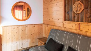 A wooden interior with a round mirror, a wooden wall panel, and a sofa with a geometric-patterned cushion. - Val Thorens - Cozy apartment for 4, ski-in/ski-out, elevator (Val Thorens)