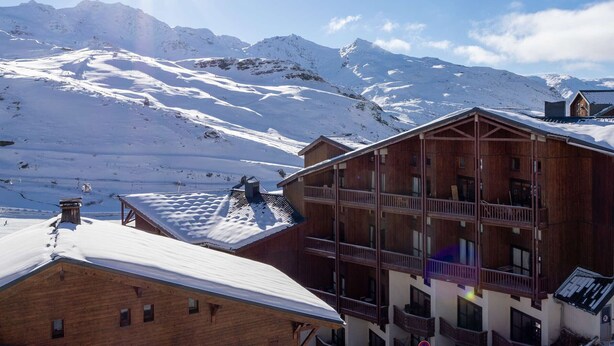 A wooden building with multiple balconies and a snow-covered mountain in the background. - Val Thorens - Cozy apartment for 4, ski-in/ski-out, elevator (Val Thorens)
