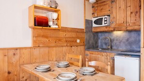 A wooden kitchen with a dining table set for four, a microwave, a sink, and a small refrigerator. - Val Thorens - Cozy apartment for 4, ski-in/ski-out, elevator (Val Thorens)