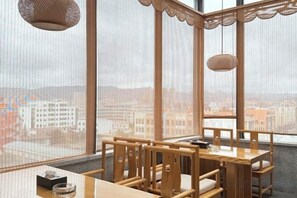 A corner dining area with a wooden table and chairs, a hanging light fixture, and a view of a cityscape through large windows.