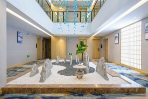 A hotel lobby with a central garden, a reception desk, and a seating area.