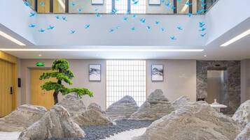 Un vestíbulo con jardín de rocas, un bonsái y una escalera decorada con adornos de pájaros azules.