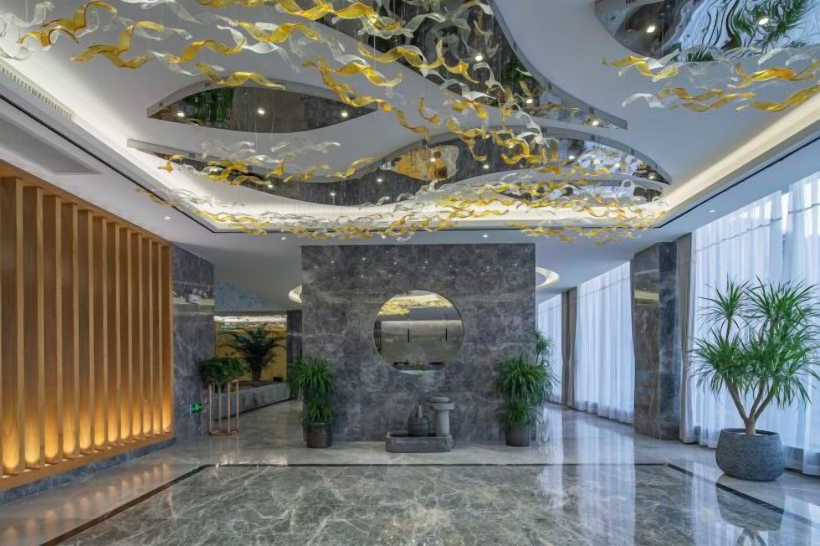 A modern lobby with a marble floor, a central column with a mirror, and a ceiling with gold leaf accents.