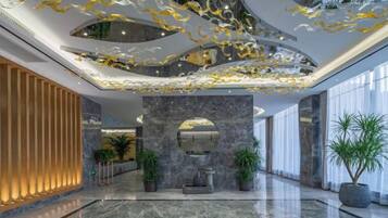 A modern lobby with a marble floor, a central column with a mirror, and a ceiling with gold leaf accents.