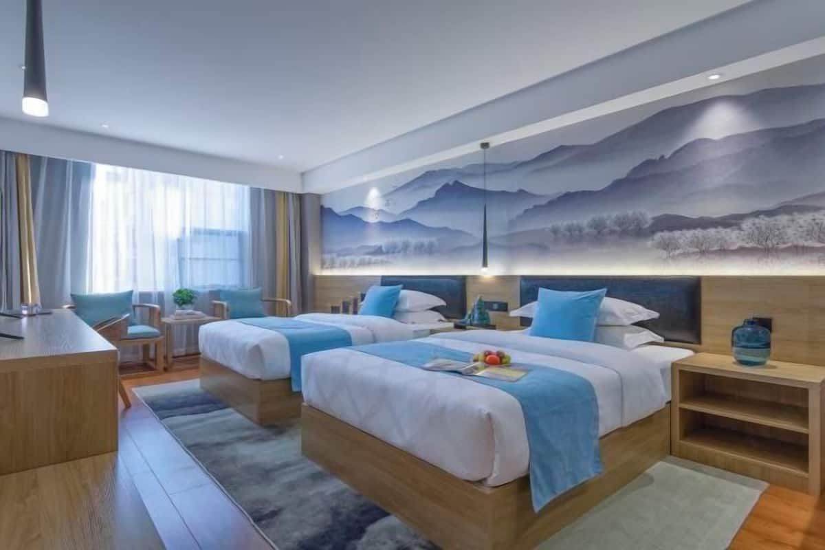A hotel room with two beds, a desk, and a mural of mountains.