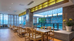 A modern dining area with wooden tables and chairs, large windows, and a view of the city. - Manyuegu Holiday Hotel (Xiangyun)