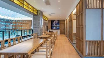 A restaurant interior with long wooden tables and chairs, a glass railing overlooking a snowy outdoor area, and a traditional Japanese-style partition on the right.