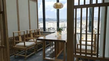 A room with a view of a cityscape, featuring a wooden table and chairs, a hanging lamp, and a window with a view.