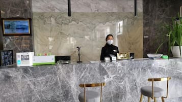 Un mostrador de recepción con encimera de mármol, un menú enmarco y una pantalla digital. Hay dos sillas con patas de madera y asientos acolchados.