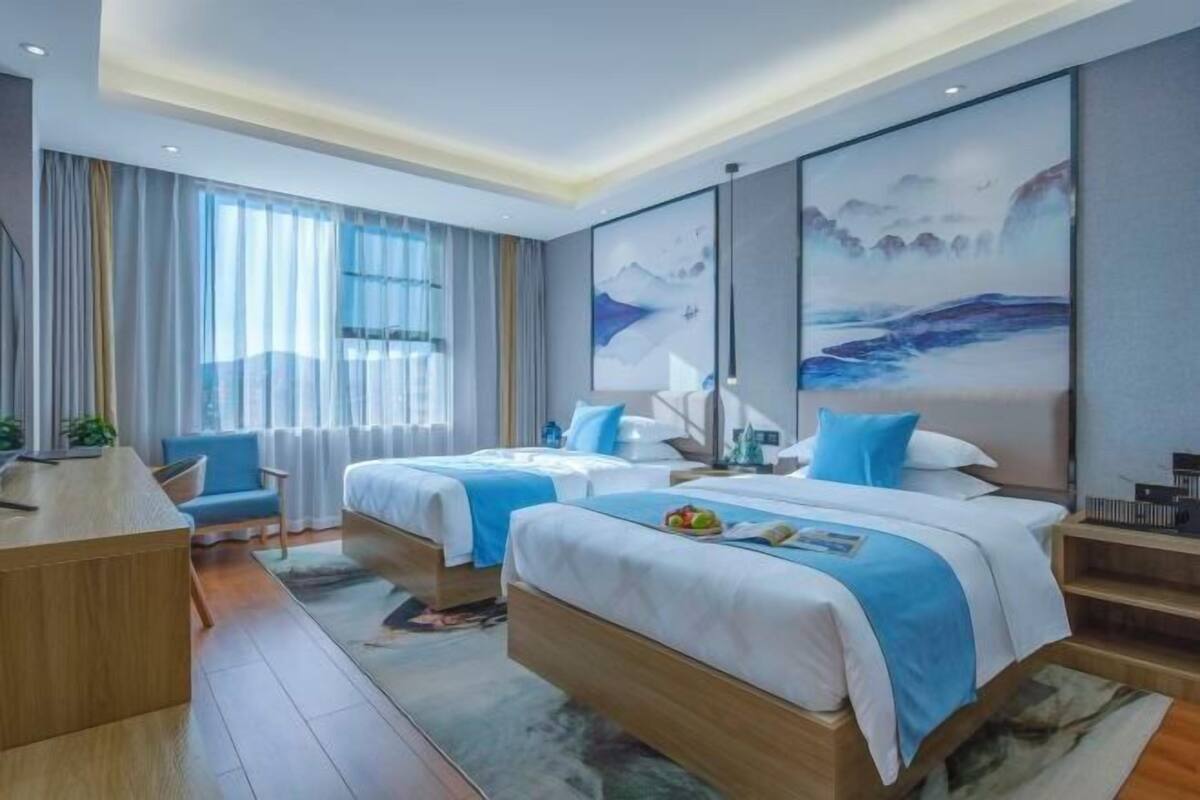 A modern hotel room with two beds, a desk, and a view of the mountains.