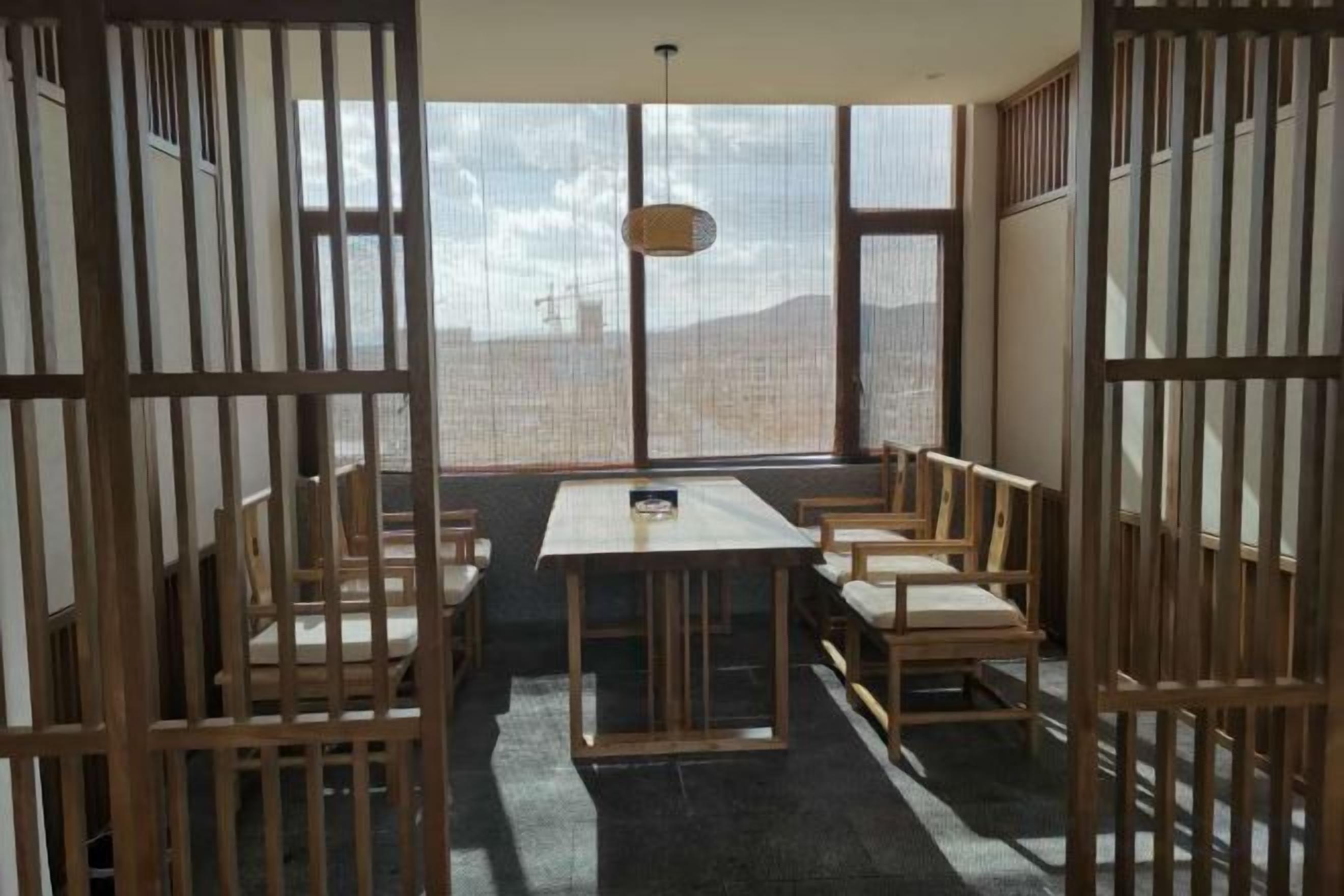 A room with a low table and benches, large windows, and a view of the outdoors.