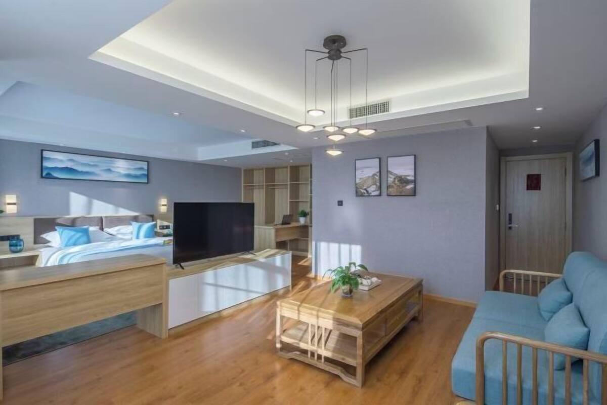 A modern living room with a flat-screen TV, wooden furniture, and a ceiling with recessed lighting.