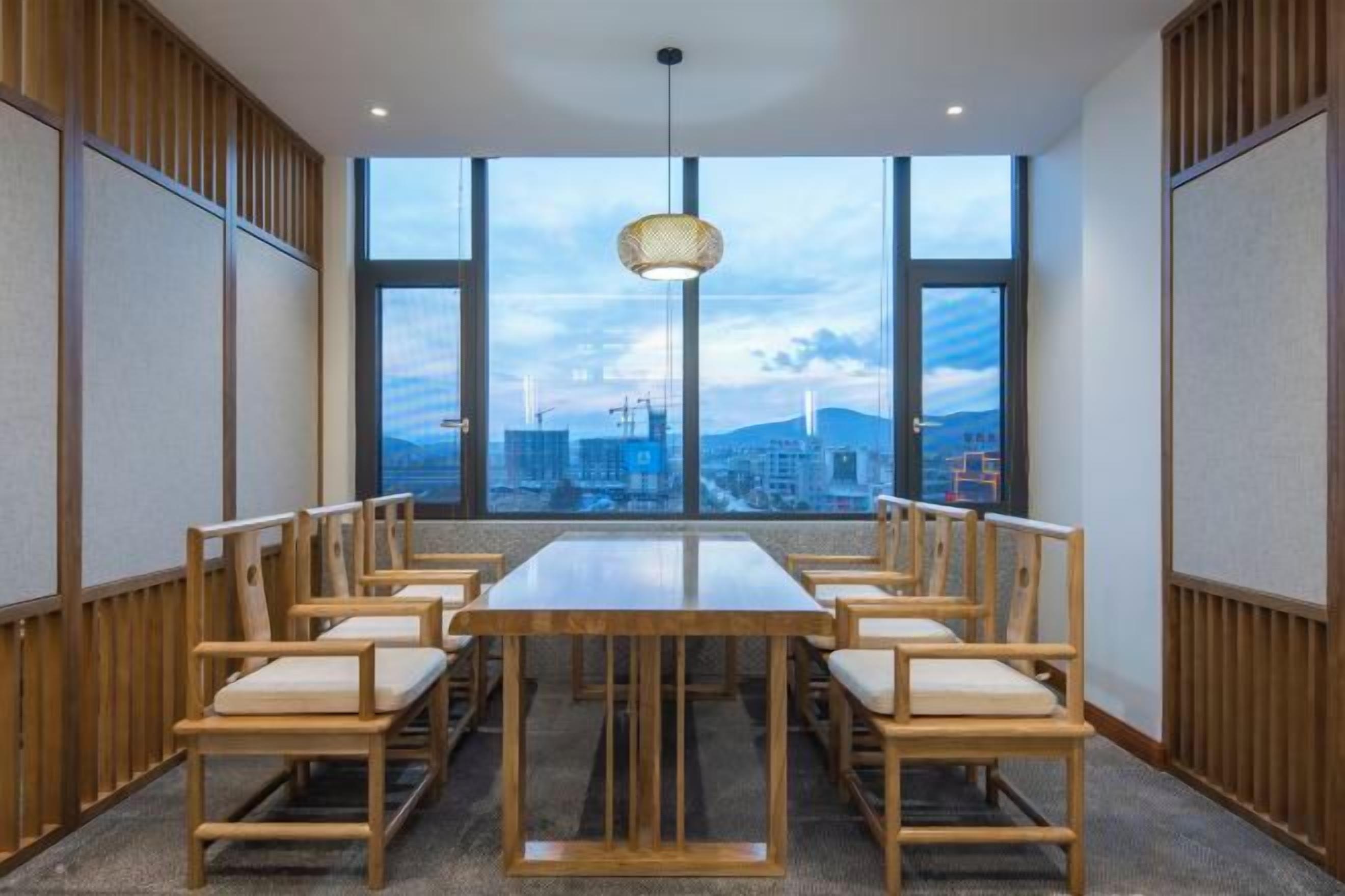 A conference room with a large table and chairs, large windows with a city view, and a hanging light fixture.