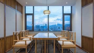 A conference room with a large table and chairs, large windows with a city view, and a hanging light fixture.