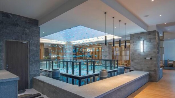 A modern hotel lobby with a glass-enclosed pool, a reception desk, and a staircase leading to an upper level. - Manyuegu Holiday Hotel (Xiangyun)