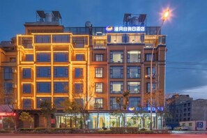 A multi-story hotel with a modern facade, illuminated windows, and a visible sign indicating a restaurant on the ground floor.