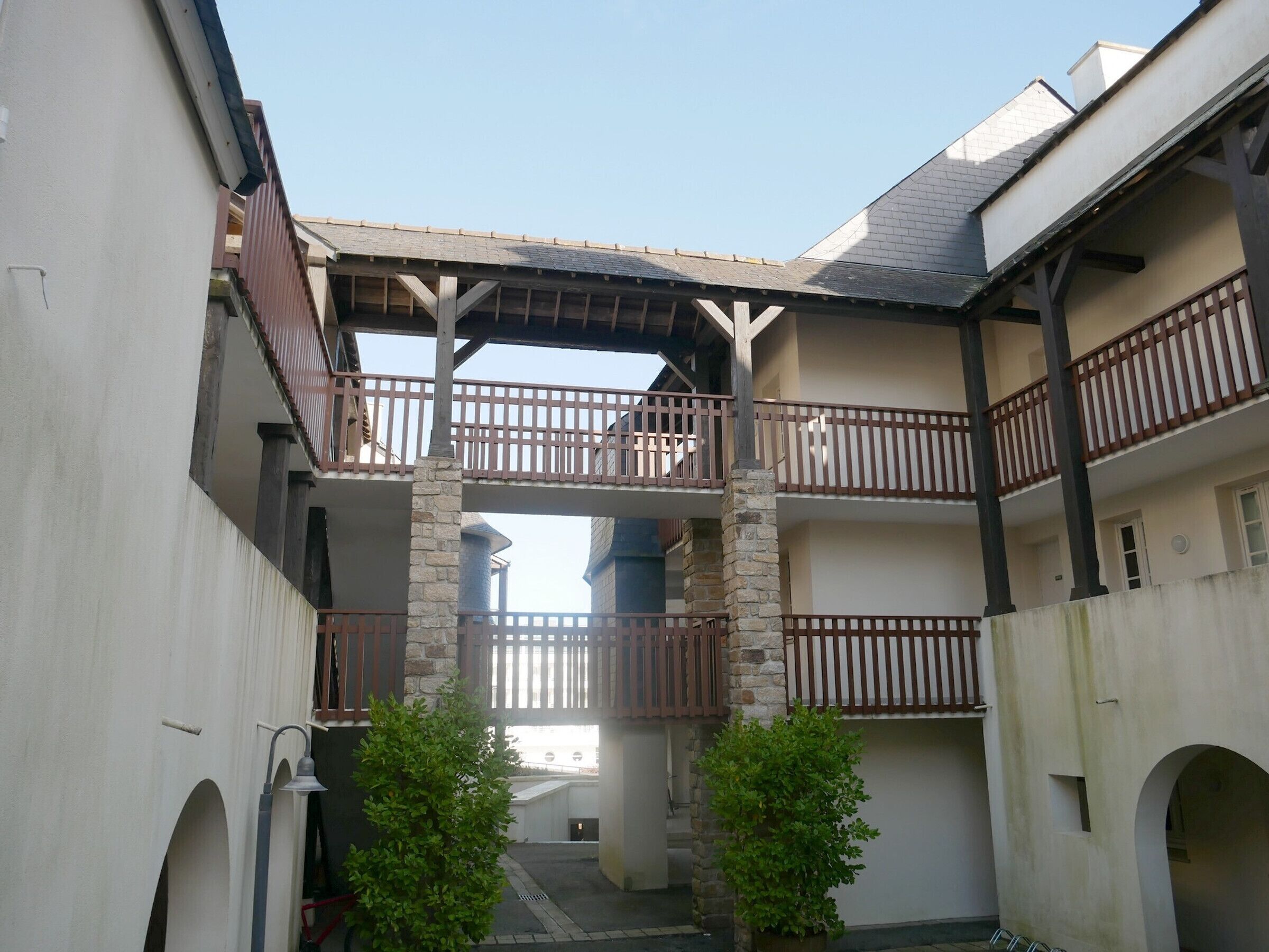 A courtyard with a central stone column, wooden balconies, and arched doorways.