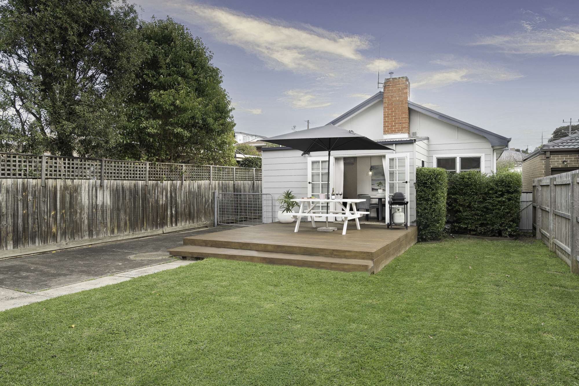 Ein Haus mit Terrasse, Grillplatz und einem umzäunten Garten.