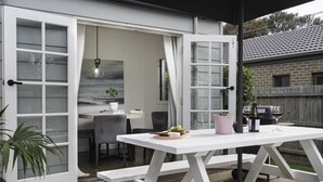Eine offene Terrasse mit einem weißen Tisch, Stühlen und einem Grill.
