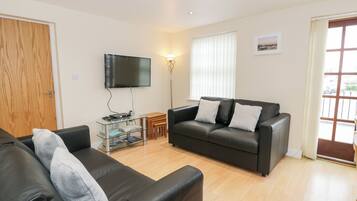 A living room with a black leather sofa, a glass coffee table, and a flat-screen TV mounted on the wall.