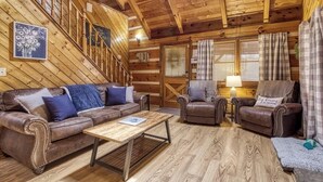 A cozy cabin interior with a wooden staircase, leather sofas, and a wooden coffee table. - Lacey's Place by Beyond Expectations: Dog-Friendly Cabin w/ Hot Tub & Fire Pit (Sevierville)