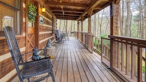 A wooden porch with a railing, benches, and a hanging plant. - Lacey's Place by Beyond Expectations: Dog-Friendly Cabin w/ Hot Tub & Fire Pit (Sevierville)