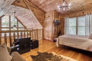 Un dormitorio de cabaña de madera con una cama, un escritorio, una silla y un ventanal grande.