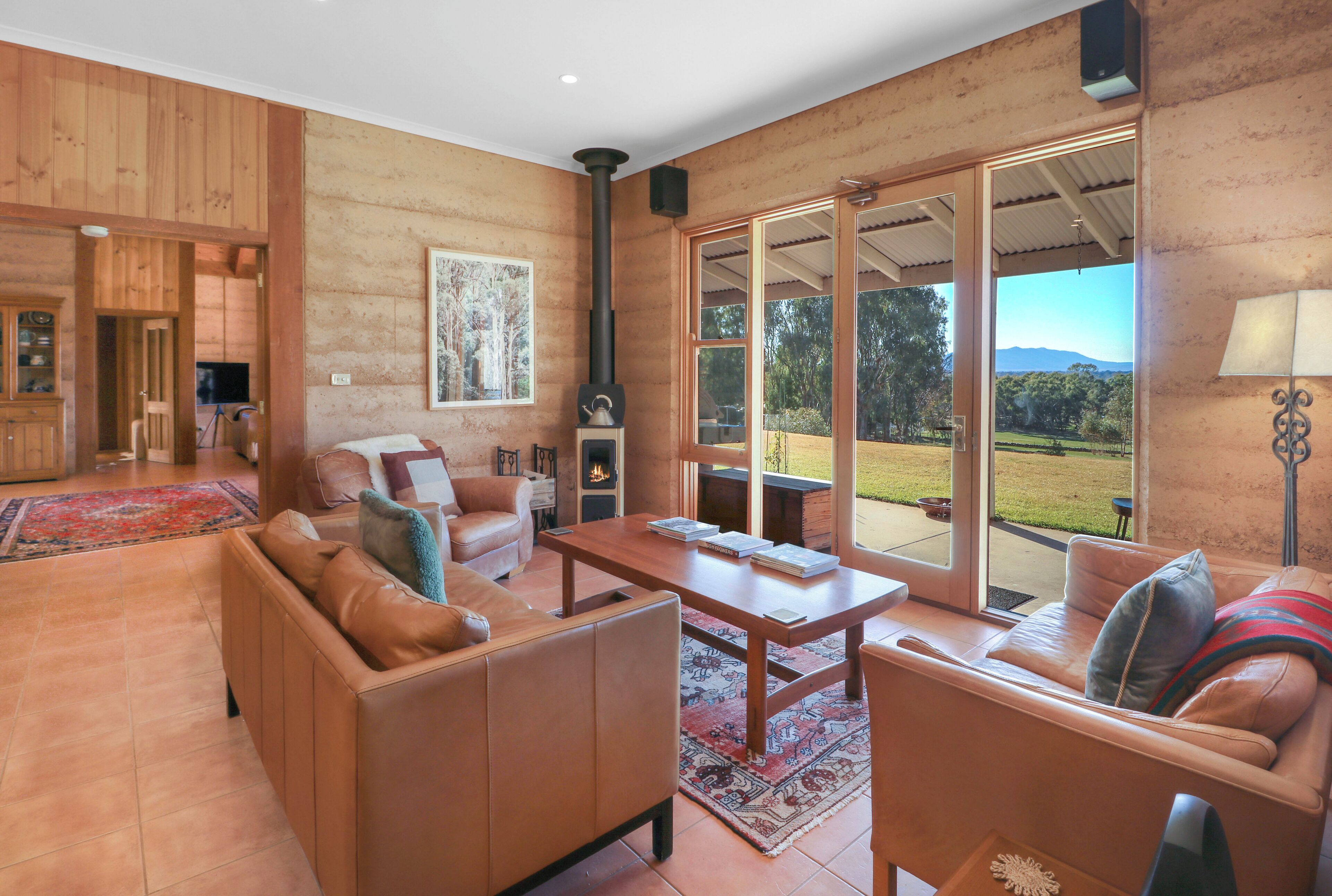 A spacious living room with a fireplace, leather sofas, a wooden coffee table, and large windows offering a view of the outdoors.