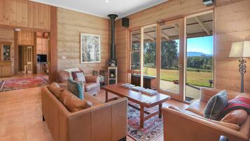 A spacious living room with a fireplace, leather sofas, a wooden coffee table, and large windows offering a view of the outdoors.