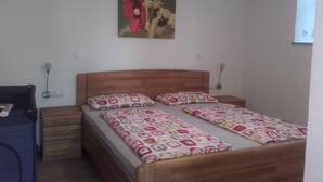 A bedroom with a wooden bed, patterned bedspread, a wall-mounted painting, bedside lamps, and a small wooden nightstand.