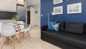 Un salon moderne avec un canapé noir, des chaises blanches, une table à manger et des œuvres d’art encadrées accrochées au mur.