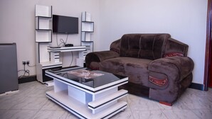 Ein Wohnzimmer mit einem flachbildfernseher an einer weißen Unterhaltungsecke, einem braunen Sofa mit roten Akzenten und einem Glastisch.