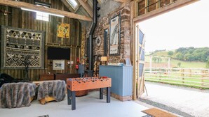 A rustic interior with a foosball table, patterned rugs, and a stone wall. - Pen Bont Home Farm (Brecon)