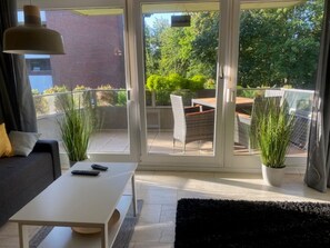 En moderne stue med sofa, hvidt sofabord og to plantede planter.