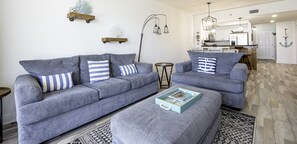 A modern living room with a grey sofa set, a coffee table, and a kitchen in the background. - Ariel Dunes I 1207 Beach Access*3 pools* (Miramar Beach)