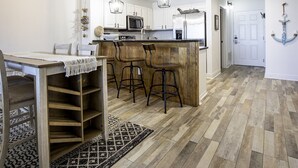 A kitchen with a wooden island, bar stools, and a dining table with chairs. - Ariel Dunes I 1207 Beach Access*3 pools* (Miramar Beach)