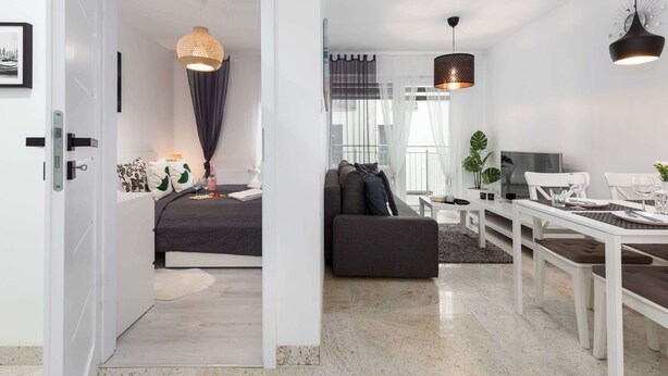 A modern living room with a sofa, dining table, and pendant lights. - Modern Apartment | Separate Bedroom and Balcony (Kołobrzeg)