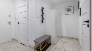 A hallway with white doors, a bench, a coat rack, and a framed leaf artwork on the wall. - Modern Apartment | Separate Bedroom and Balcony (Kołobrzeg)