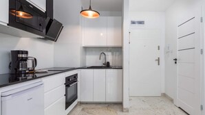 A modern kitchen with white cabinetry, a black countertop, and a built-in microwave. - Modern Apartment | Separate Bedroom and Balcony (Kołobrzeg)