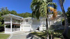 Ein zweistöckiges Haus mit überdachter Veranda, Garage und einem kleinen Garten mit Palmen.