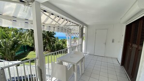 Ein Balkon mit weißem Tisch und Stühlen, Blick auf den Ozean, und eine Tür mit Fenster.