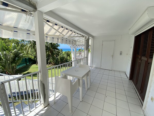 A balcony with a white table and chairs, a view of the ocean, and a door with a window.