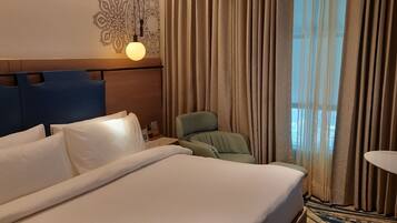 Habitación de hotel con una cama grande, una mesita de noche, un sillón verde y una pequeña mesa.