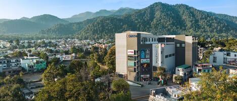A multi-story building with various commercial signs, surrounded by a residential area and hills in the background.