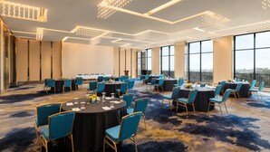Un salón de conferencias con mesas redondas, sillas azules y suelo alfombrado.