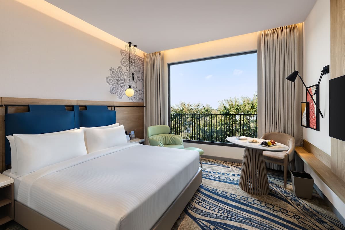 Quarto de hotel com uma cama grande, uma mesa pequena, uma cadeira, televisão e varanda com vista.