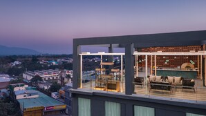 Una terraza moderna en la azotea con barandillas de cristal, mobiliario exterior y vistas a la ciudad.