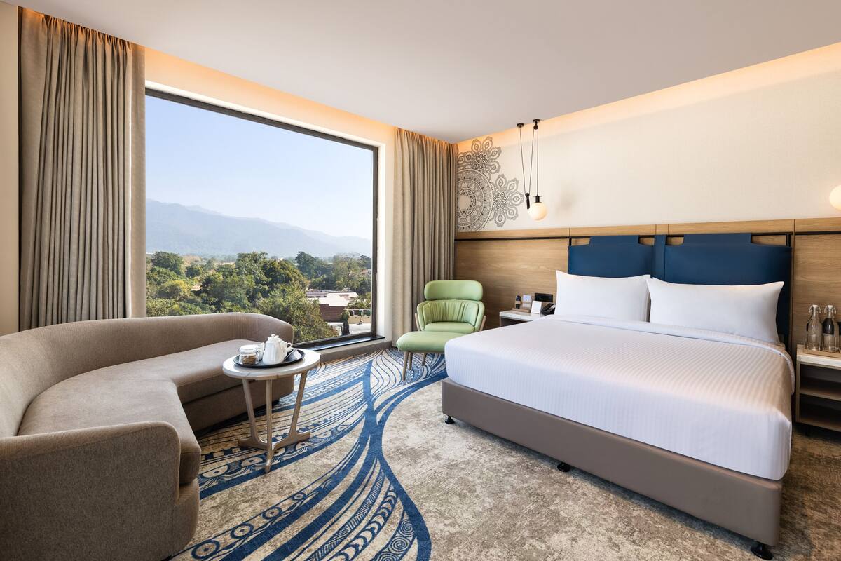 Quarto de hotel com uma cama grande, um sofá, uma mesa pequena e uma cadeira.