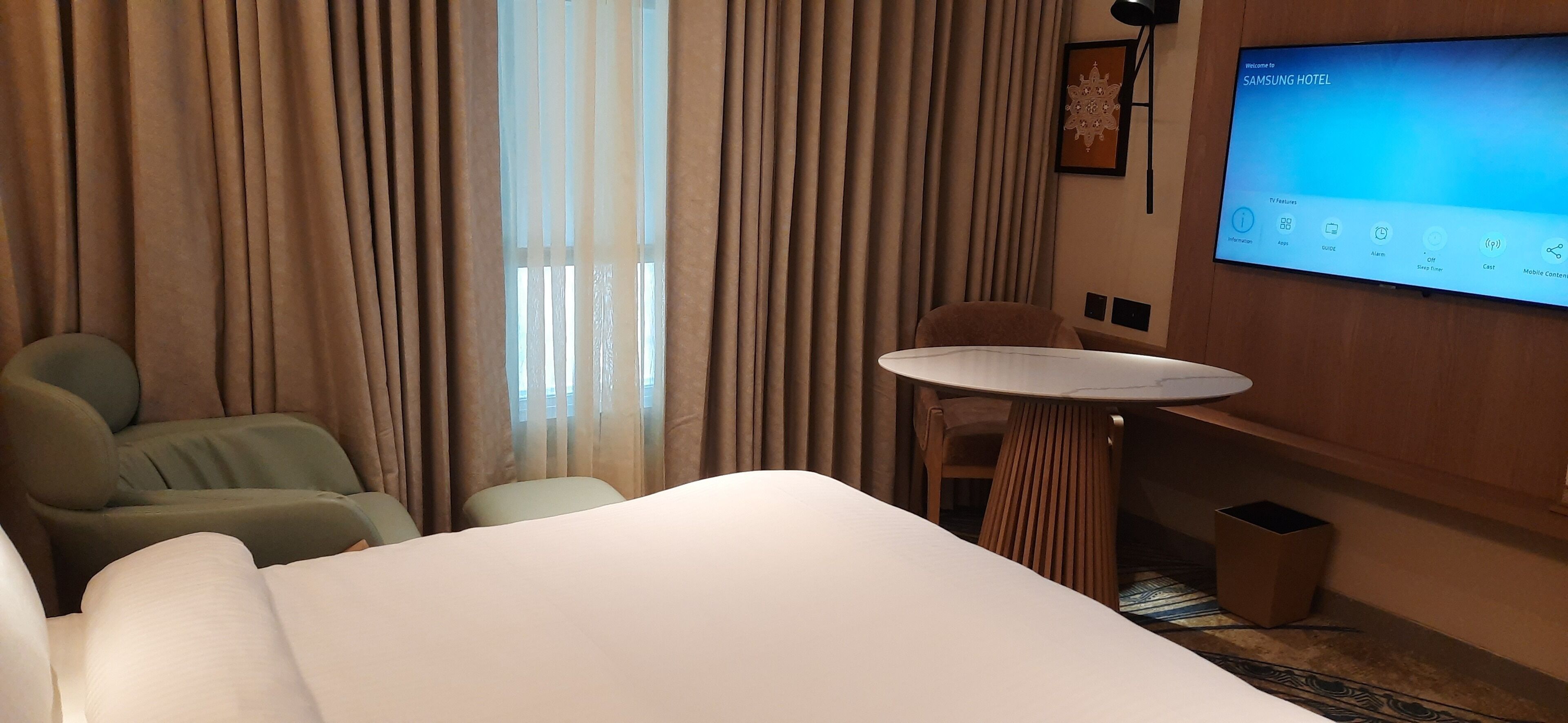 A hotel room with a bed, a small round table, a sofa, and a TV screen displaying a welcome message.